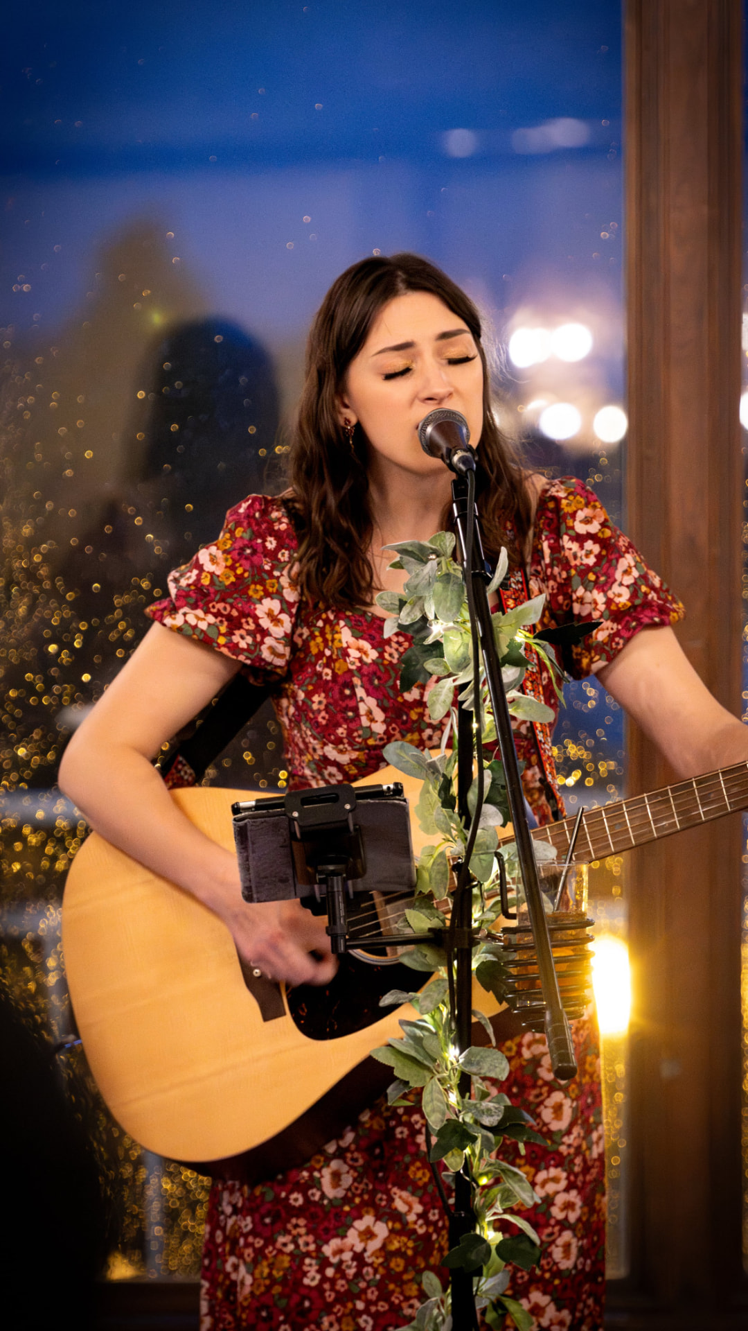 Anna Marie singing and playing guitar in a floral dress at an evening venue