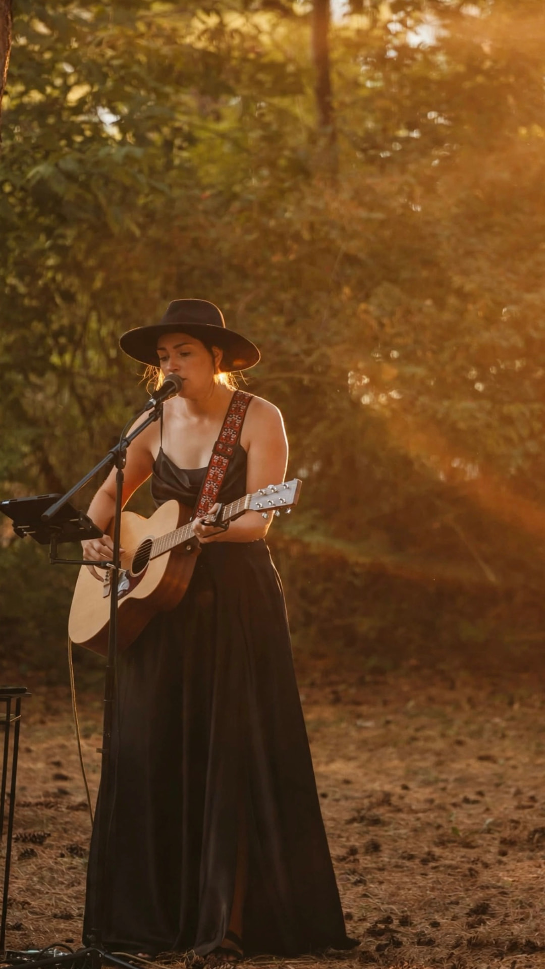 Anna Marie singing and playing guitar at an outdoor wedding ceremony at golden hour